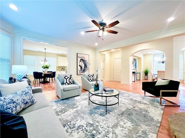 living room featuring crown molding, ceiling fan with notable chandelier, and light wood-type flooring