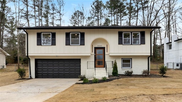 raised ranch featuring a garage, concrete driveway, and brick siding