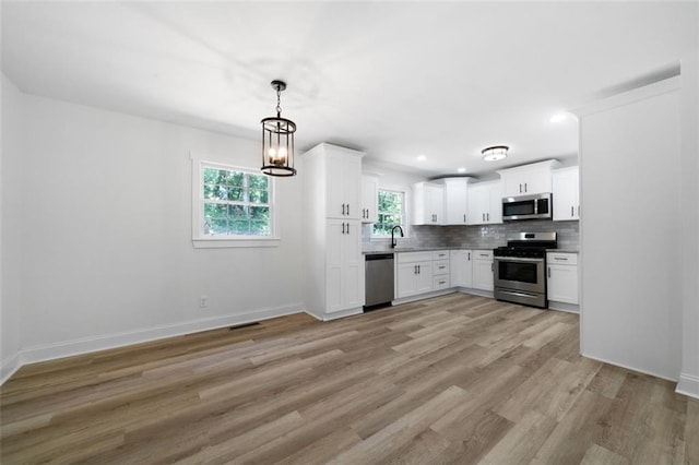 kitchen featuring stainless steel appliances, decorative backsplash, sink, white cabinetry, and an inviting chandelier