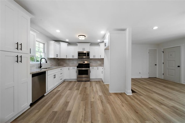 kitchen featuring stainless steel appliances, sink, white cabinetry, light hardwood / wood-style floors, and backsplash