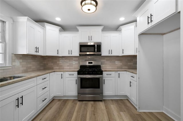 kitchen with light stone counters, appliances with stainless steel finishes, light hardwood / wood-style flooring, and white cabinetry