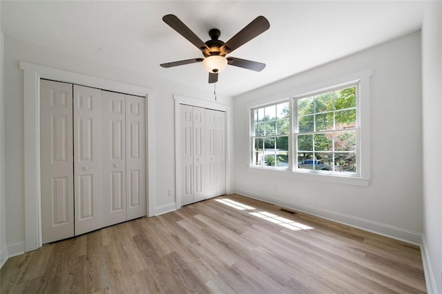 unfurnished bedroom featuring multiple closets, ceiling fan, and light hardwood / wood-style floors