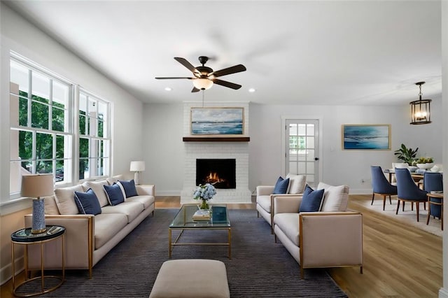 living room featuring dark wood-type flooring, a brick fireplace, and ceiling fan with notable chandelier