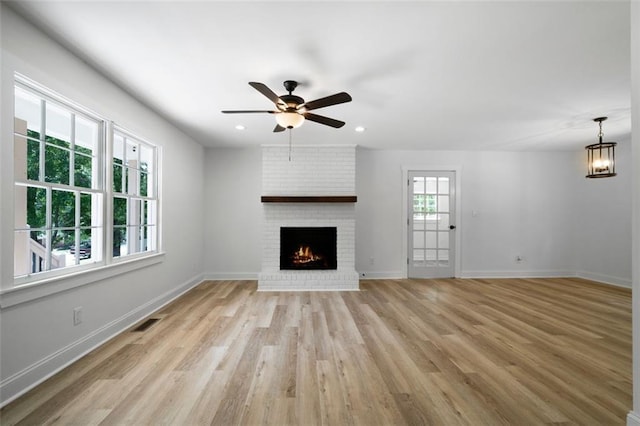 unfurnished living room with ceiling fan with notable chandelier, a brick fireplace, and light hardwood / wood-style flooring