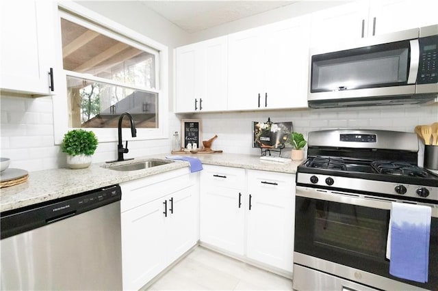 kitchen with white cabinetry, sink, light stone counters, and appliances with stainless steel finishes