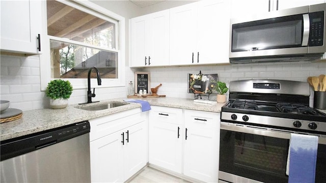 kitchen with light stone countertops, stainless steel appliances, white cabinetry, and sink