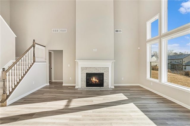 unfurnished living room featuring stairway, a towering ceiling, visible vents, baseboards, and a brick fireplace