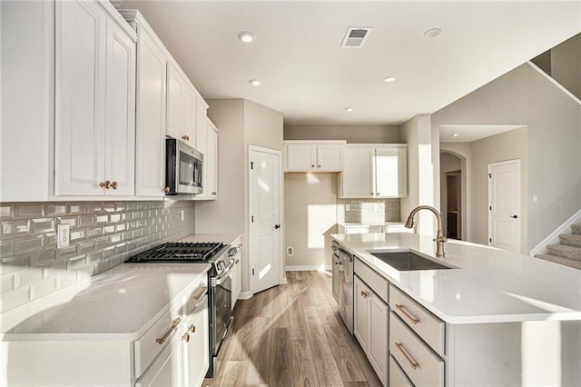 kitchen featuring a sink, light wood-style floors, a center island with sink, appliances with stainless steel finishes, and visible vents