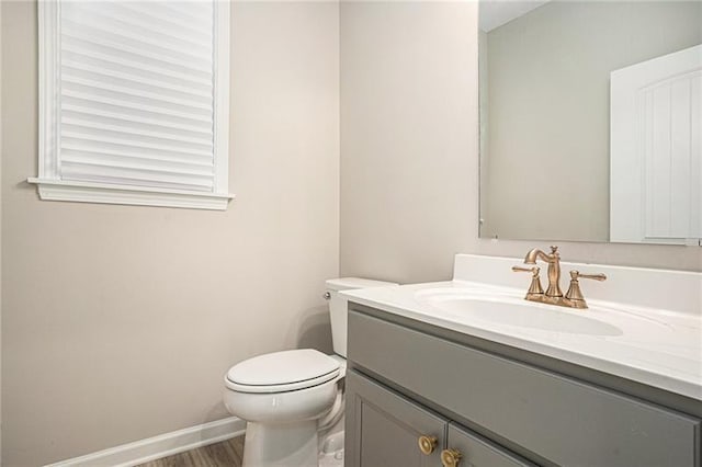 half bathroom with baseboards, wood finished floors, vanity, and toilet
