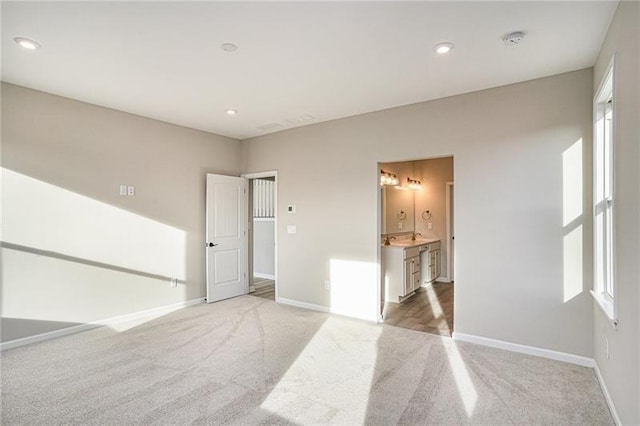 unfurnished bedroom with ensuite bath, baseboards, recessed lighting, and light colored carpet