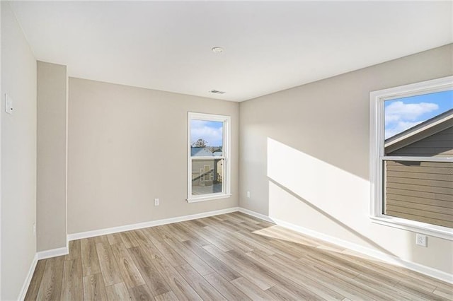 empty room featuring light wood-type flooring, a healthy amount of sunlight, baseboards, and visible vents