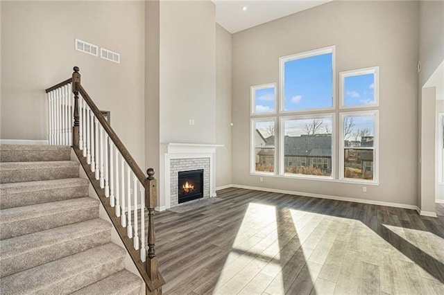 unfurnished living room featuring baseboards, wood finished floors, a towering ceiling, and a brick fireplace