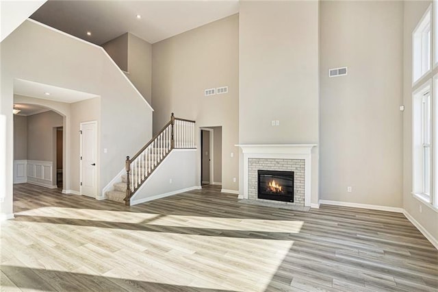 unfurnished living room featuring a towering ceiling, wood finished floors, visible vents, arched walkways, and stairs