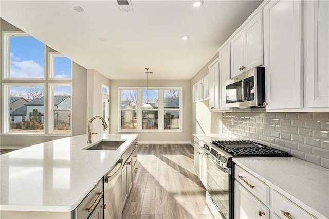 kitchen featuring a sink, light wood-style floors, stainless steel appliances, backsplash, and visible vents