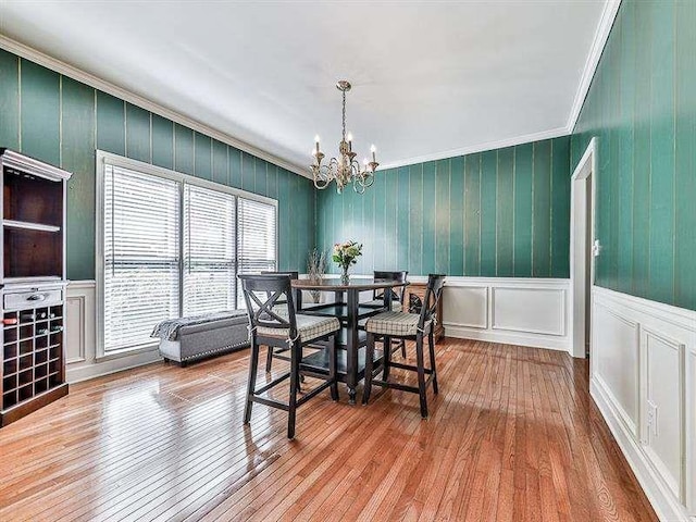 dining space with a decorative wall, ornamental molding, wood-type flooring, and a chandelier