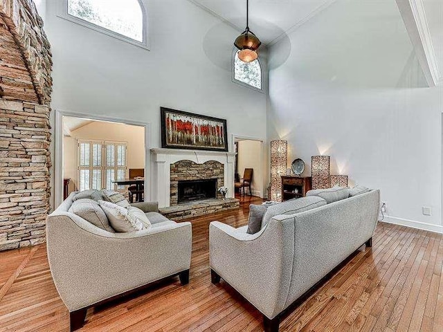 living area with a high ceiling, baseboards, light wood-style floors, and a stone fireplace