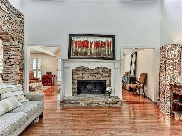 living area featuring a stone fireplace, a high ceiling, and wood finished floors