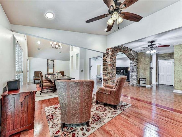 living room featuring wood finished floors, arched walkways, baseboards, ceiling fan, and ornate columns