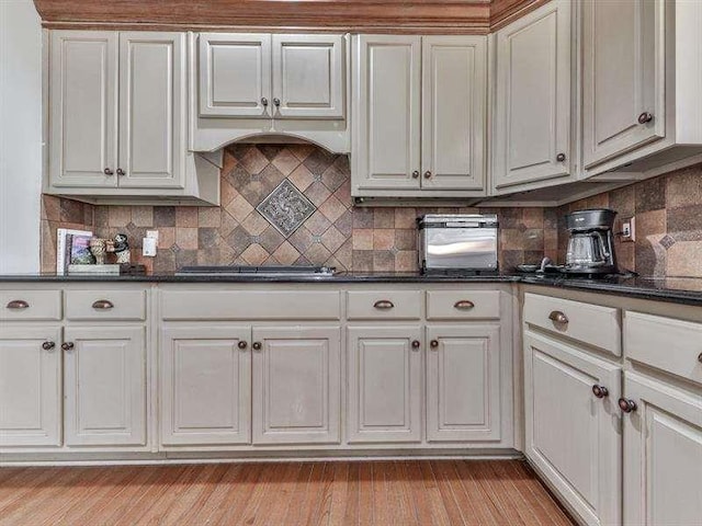 kitchen featuring cooktop, dark countertops, light wood-style flooring, and decorative backsplash