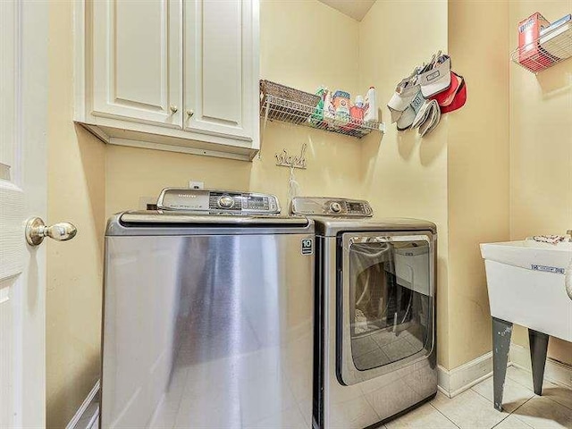 laundry area with light tile patterned flooring, cabinet space, baseboards, and washing machine and clothes dryer