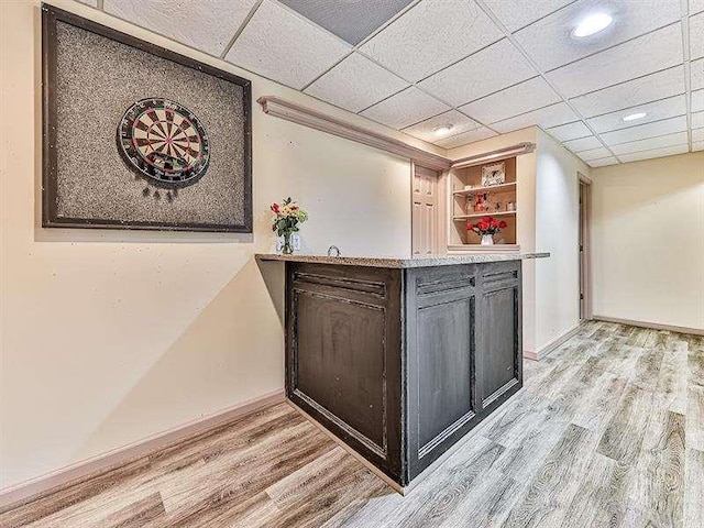 bar with light wood-type flooring, a paneled ceiling, and baseboards