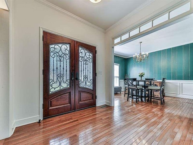 entrance foyer featuring ornamental molding, french doors, wood-type flooring, a decorative wall, and a chandelier