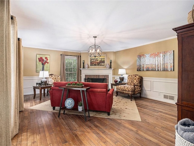 living room with crown molding, a fireplace, a notable chandelier, and hardwood / wood-style flooring