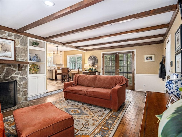 living room with a fireplace, beamed ceiling, wood-type flooring, and french doors