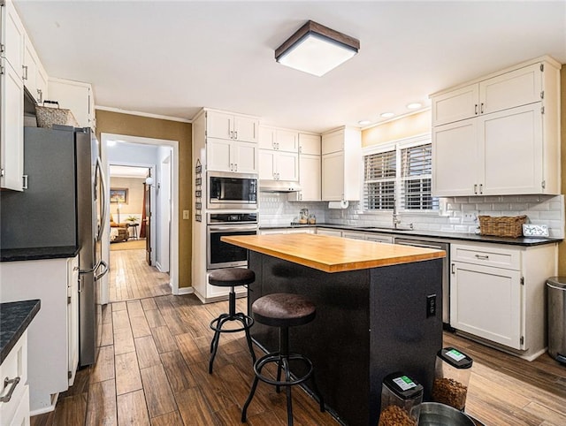 kitchen with tasteful backsplash, white cabinetry, hardwood / wood-style floors, and appliances with stainless steel finishes