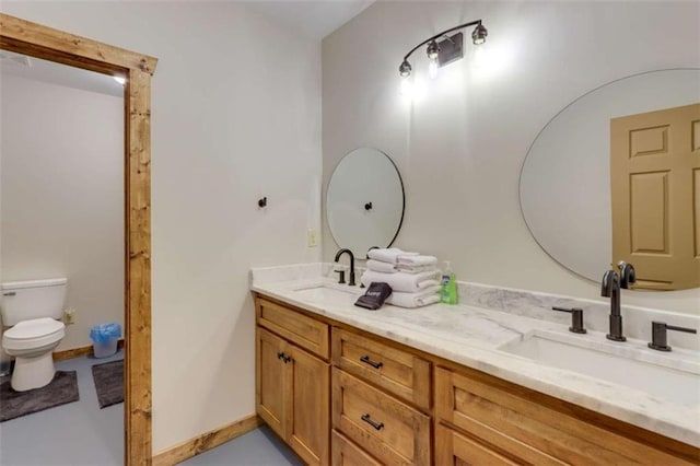 bathroom featuring double vanity, a sink, toilet, and baseboards