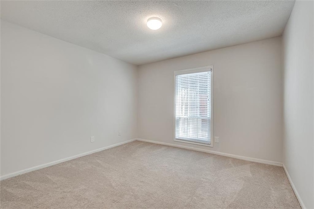 spare room with light colored carpet, a textured ceiling, and baseboards