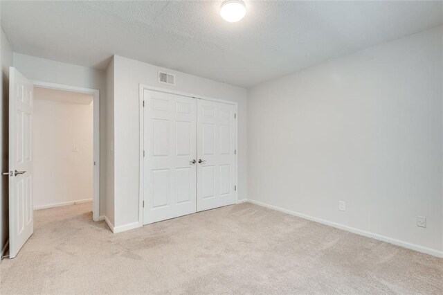 unfurnished bedroom with a textured ceiling, light colored carpet, visible vents, baseboards, and a closet