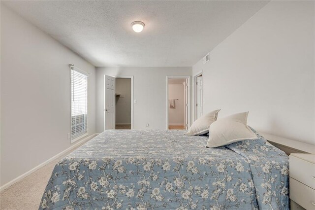 carpeted bedroom with a textured ceiling, ensuite bathroom, visible vents, baseboards, and a spacious closet