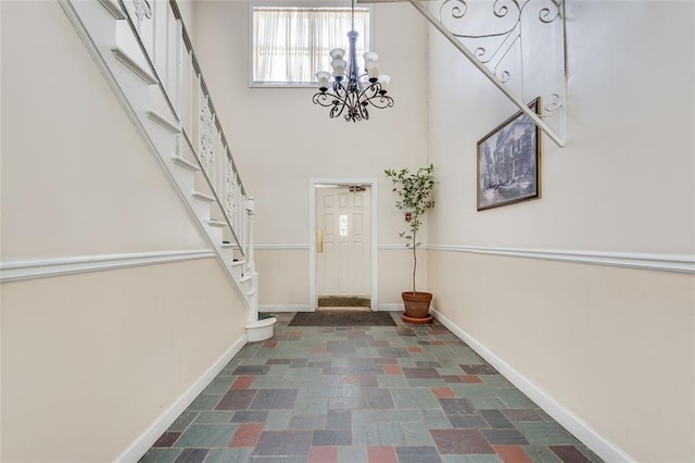 foyer entrance with a high ceiling, stairs, baseboards, and a chandelier