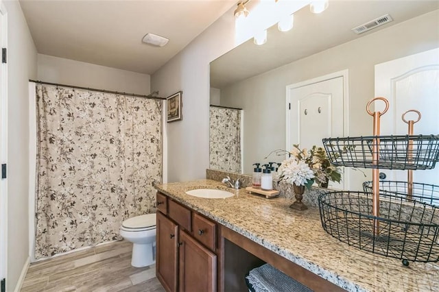 bathroom featuring hardwood / wood-style floors, walk in shower, vanity, and toilet