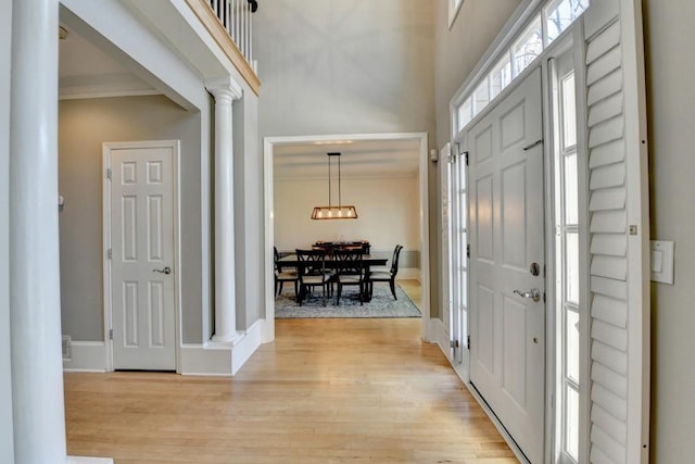 foyer featuring a high ceiling, light wood-type flooring, decorative columns, and ornamental molding