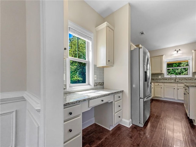 kitchen featuring stainless steel refrigerator with ice dispenser, dark hardwood / wood-style floors, light stone countertops, built in desk, and tasteful backsplash