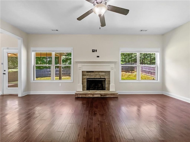 unfurnished living room featuring ceiling fan, a fireplace, a wealth of natural light, and dark wood-type flooring