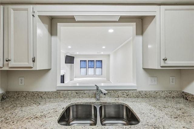 kitchen with a fireplace, light stone counters, a sink, and recessed lighting