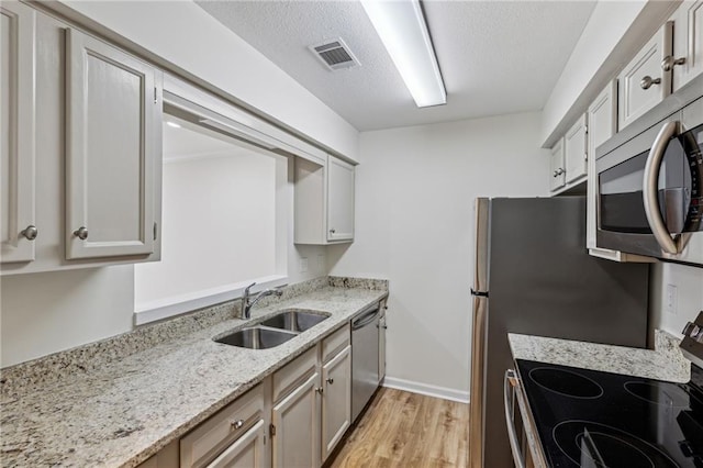 kitchen with stainless steel appliances, visible vents, light wood-style flooring, a sink, and light stone countertops