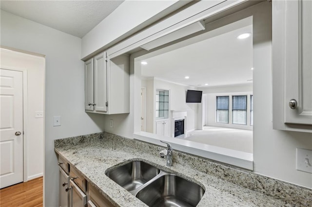 kitchen with a fireplace, recessed lighting, a sink, light stone countertops, and light wood-type flooring