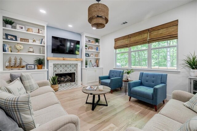 living room featuring a fireplace, visible vents, built in shelves, and light wood-type flooring