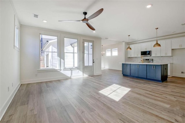 kitchen featuring appliances with stainless steel finishes, white cabinets, hanging light fixtures, a kitchen island with sink, and blue cabinetry