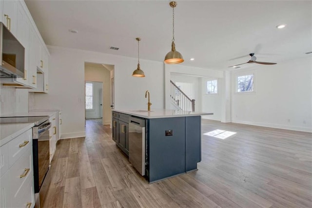 kitchen with sink, appliances with stainless steel finishes, white cabinetry, a kitchen island with sink, and decorative light fixtures