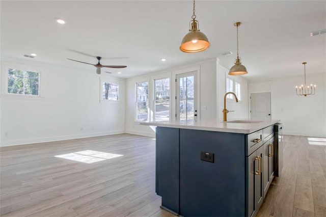 kitchen with sink, hanging light fixtures, a center island with sink, light hardwood / wood-style floors, and ceiling fan with notable chandelier