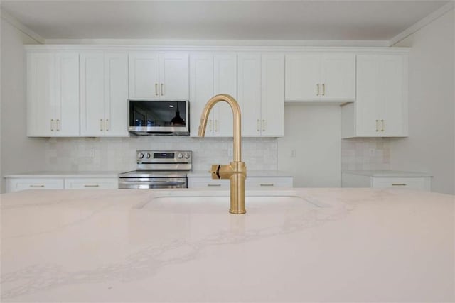 kitchen featuring stainless steel appliances, light stone countertops, decorative backsplash, and white cabinets