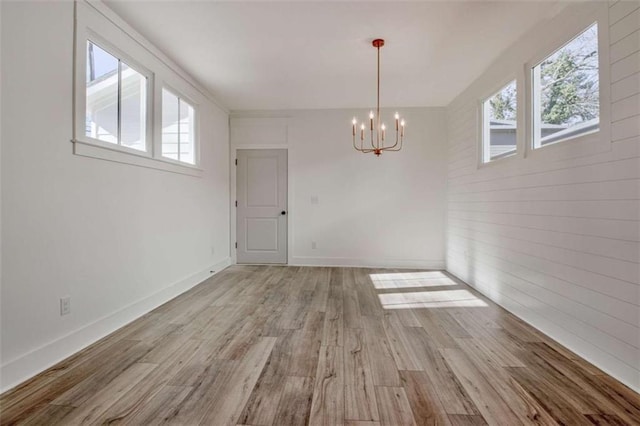 unfurnished dining area featuring a healthy amount of sunlight, an inviting chandelier, and light wood-type flooring