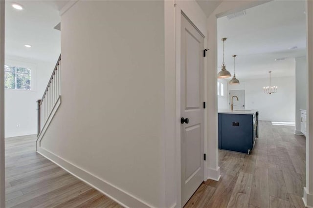 hallway featuring an inviting chandelier, sink, and light hardwood / wood-style floors