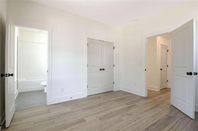 unfurnished bedroom featuring ensuite bath, a closet, and light wood-type flooring