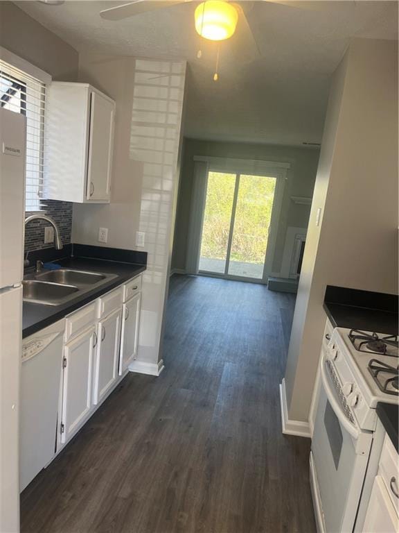 kitchen with white appliances, dark countertops, dark wood-style flooring, white cabinetry, and a sink